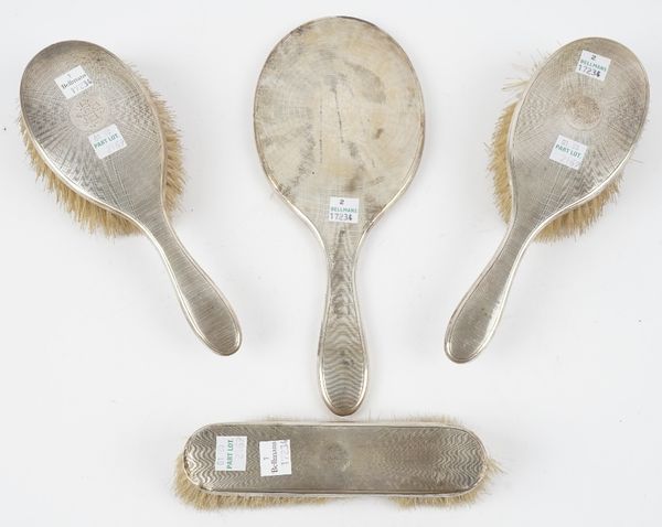 A silver mounted four piece part dressing set, comprising; a hand mirror, a pair of hairbrushes and a clothes brush, all having engine turned decorati