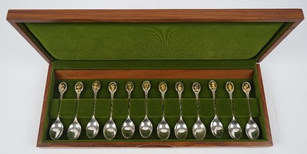 A set of twelve silver floral decorated spoons, the finials with applied gilt oval differing floral motifs, with accompanying paperwork and fitted woo