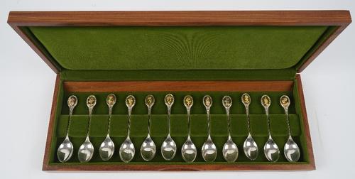 A set of twelve silver floral decorated spoons, the finials with applied gilt oval differing floral motifs, with accompanying paperwork and fitted woo