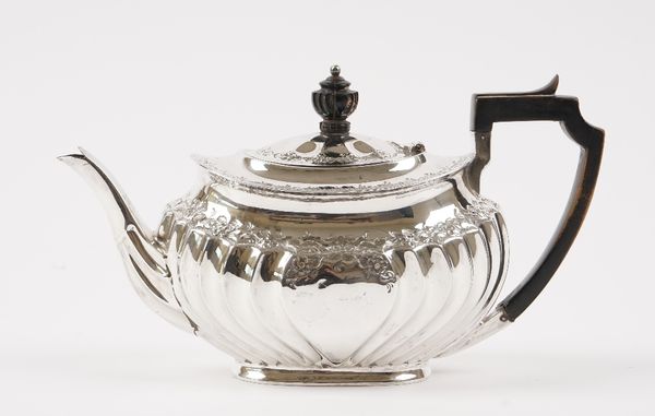 A silver teapot, of oval form with partly fluted decoration below a floral and foliate decorated rim, with ebonised fittings, raised on an oval foot,