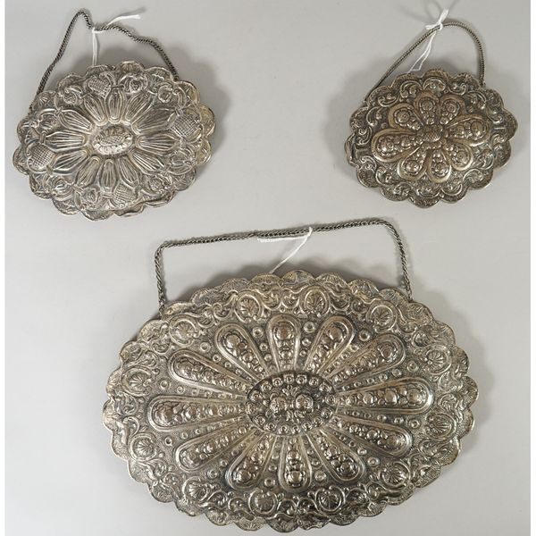 A Turkish shaped oval mirror, with embossed decoration, fitted with a chain, width 30.5cm and two smaller Turkish shaped oval mirrors, fitted with cha