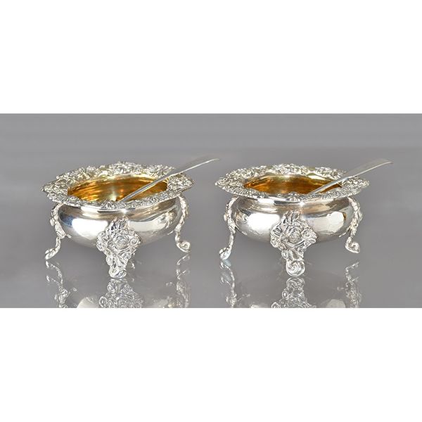 A pair of George III silver salts, each of shaped circular form, decorated with a floral and scalloped wide rim, gilt within and raised on four foliat