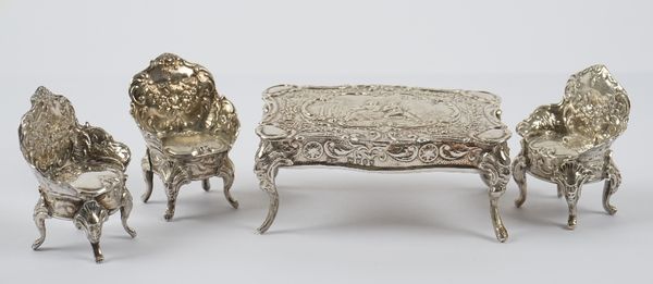 A group of miniature silver furniture, comprising; a shaped rectangular table, decorated with figures within a floral surround, import mark London 189