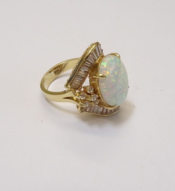 A gold, synthetic opal and colourless gem set ring, claw set with the oval cut synthetic opal to the centre, within a colourless gem set surround (one