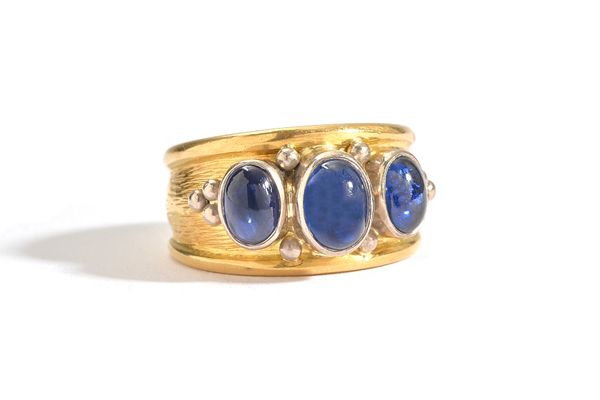 An 18ct gold and sapphire three stone ring, collet set with a row of three oval cabochon sapphires, with bead motifs at intervals, on a textured groun