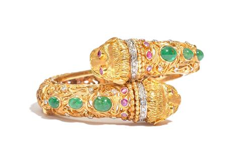 An emerald, ruby and diamond hinged bangle by Ilias Lalaounis, the hinged open work bangle of crossover design, each end modelled as a lion's head, se
