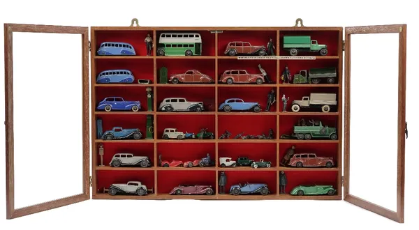 Twenty-four pre-war Dinky die-cast vehicles and related items in a glazed mahogany wall cabinet, 57cm wide.