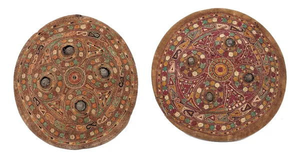 Two Indian Dhal shields, with embroidered covers with a repeated design on a maroon and rust ground, each 29cm diameter, (2).