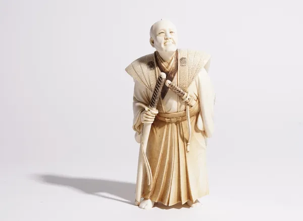 A Japanese ivory okimino of a samurai, the elderly warrior carved standing with katana and wakizashi, signed on red lacquer reserve, 18cm high.