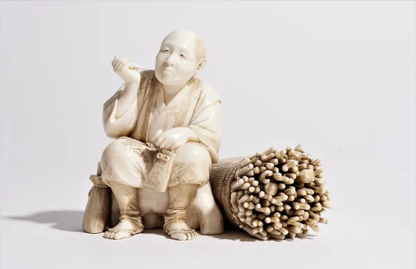 A Japanese ivory okimono of a woodcutter, Meiji/Taisho period, carved seated with a pipe and tobacco pouch, a bundle of twigs at his side, signed, 9cm