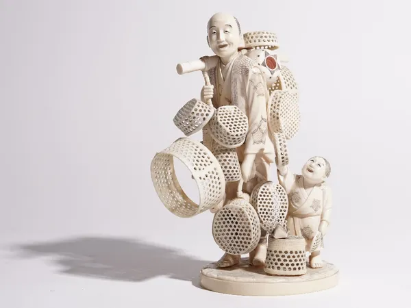 A Japanese ivory okimono of a street vendor, Meiji period, standing with a bamboo pole over his right shoulder from which baskets are suspended, a boy