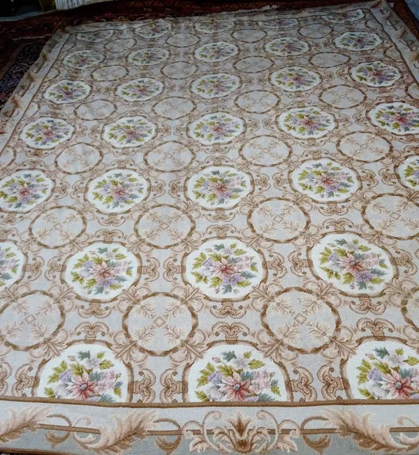 A tapestry carpet of European design, the field with rows of connecting ivory roudels, each bearing a floral bouquet; a leaf border, 294cm x 237cm.