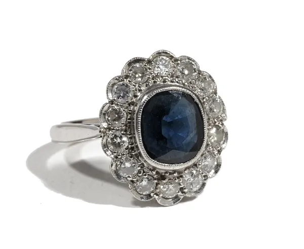 An 18ct gold, sapphire and diamond cluster ring, the central cushion-cut sapphire, collet-set in a white gold mount, with a surround of circular cut d