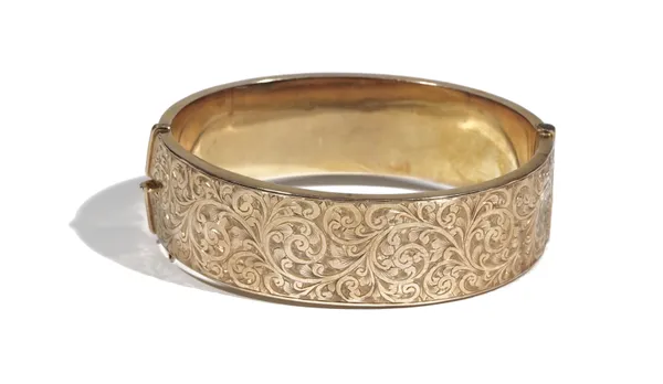 A 9ct gold hinged bangle, of oval hollow design, engraved to one side with scrolling foliage, to a concealed box and tongue clasp, 20.4g gross.