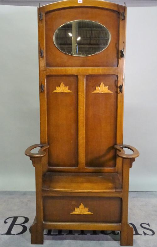 An early 20th century arts and crafts oak hall stand with an oval mirrored back lift top seat, 85cm wide x 120cm high.