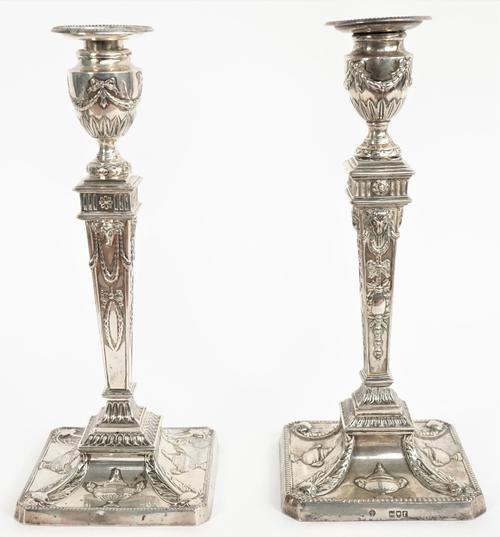 Two similar silver table candlesticks, each with a tapered square section stem, raised on a cut cornered square base, decorated with pendant swags to