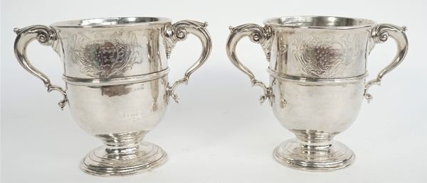 A pair of silver twin handled cups, each body decorated with a central band, with scrolling handles, raised on a circular foot, the bodies engraved wi