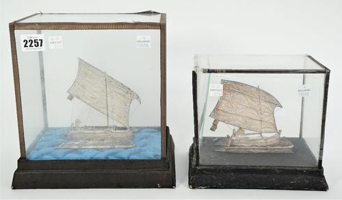 Two filigree models of South East Asian single masted sailing vessels, displayed in individual glazed cases, length of bases 22.5cm and 19cm, (2).
