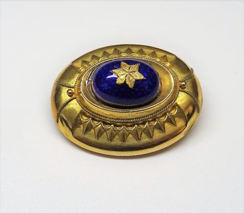 A Victorian gold and blue enamelled oval brooch, circa 1860, with applied bead and wirework decoration, glazed with a locket compartment at the back.