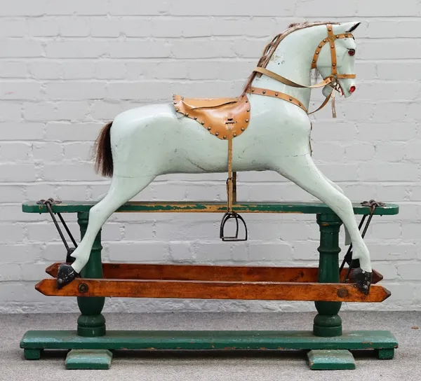 An early 20th century green painted wooden rocking horse with a tan saddle and glass eyes, 125cm wide and 113cm high.