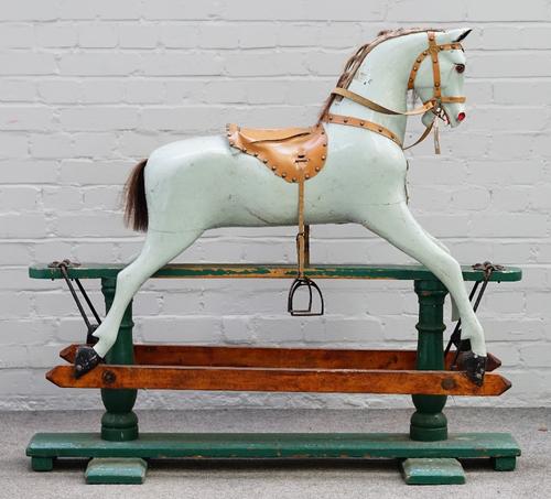 An early 20th century green painted wooden rocking horse with a tan saddle and glass eyes, 125cm wide and 113cm high.