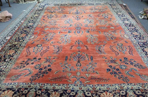 A Sarough carpet, Persian, the madder field with allover floral sprays; an indigo palmette and floral spray border, 404cm x 314cm.