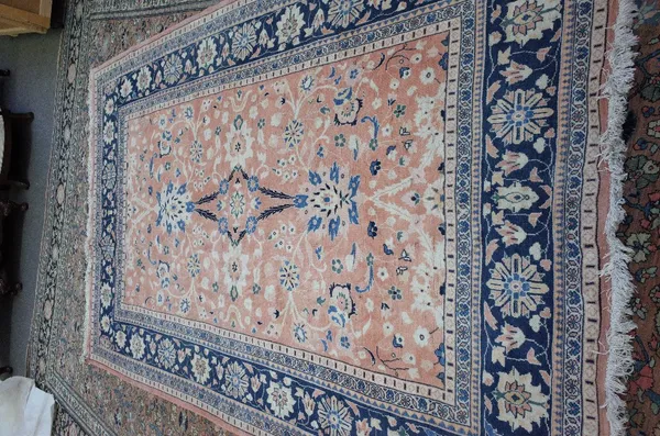 A Persian rug, the pale madder field with two bold palmettes and floral sprays, an indigo palmette and rosette border, 298cm x 192cm.