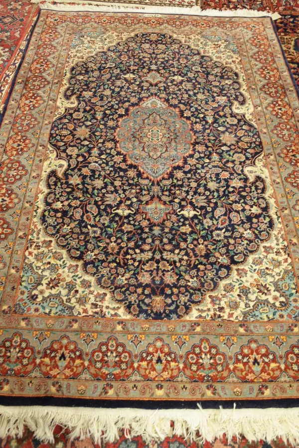 An Indian rug of Persian design, the dark indigo field with a pale medallion, ivory spandrels, all with intricate floral sprays; a madder shaped borde