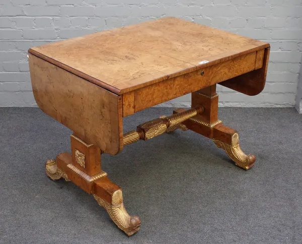 A Regency parcel gilt burr elm and elm banded sofa table, with single frieze drawer on trestle supports and leaf scroll feet, united by spiral turned