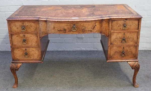 A figured walnut bowfront writing desk of George II style, with seven drawers about the knee on shell capped supports, 124cm wide x 75cm high.