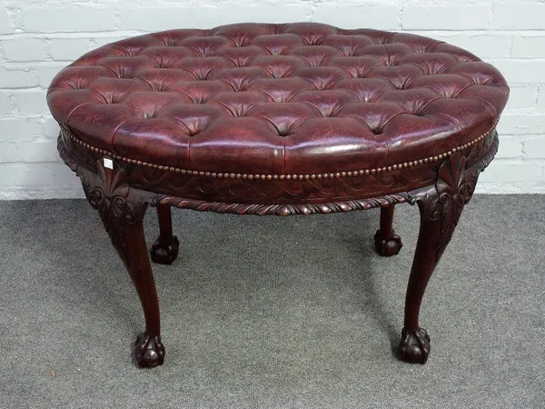 An 18th century style footstool, the oval leather upholstered top over carved frieze, on four ball and claw supports, 90cm wide x 60cm high.