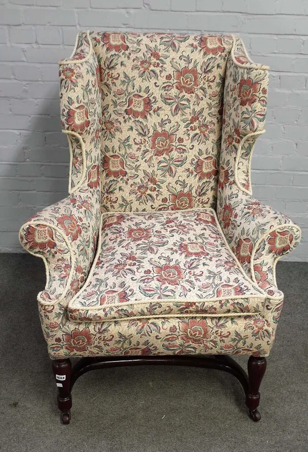 A 19th century Queen Anne style shaped wingback armchair, on turned mahogany supports, united by X-frame stretcher, 90cm x 117cm high.