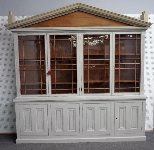 A grey painted bookcase cabinet, with architectural cornice fitted with novelty chimney pots over four glazed doors and four panelled cupboards on a p