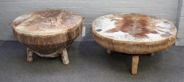 An African circular kettle drum table on three block supports, 95cm diameter x 47cm high, together with another smaller, 78cm diameter x 50cm high.