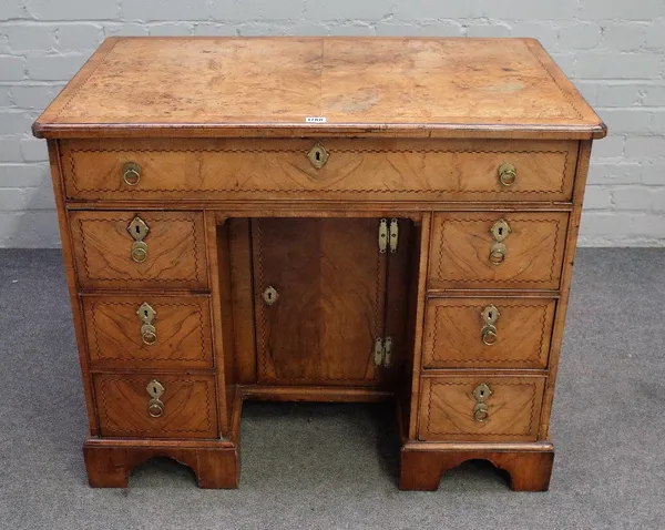 A Queen Anne walnut veneered chequer banded kneehole desk, the moulded edge quarter veneered crossbanded top above a fitted long frieze drawer, six pe