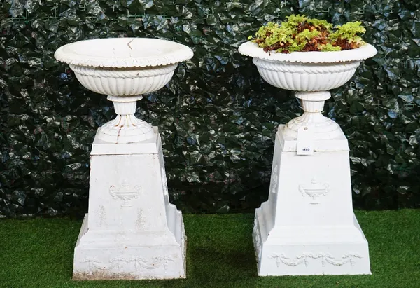 A pair of white painted cast iron campana shape terrace urns, late 19th century, with egg and tongue rims, on spreading square plinth bases, the sides