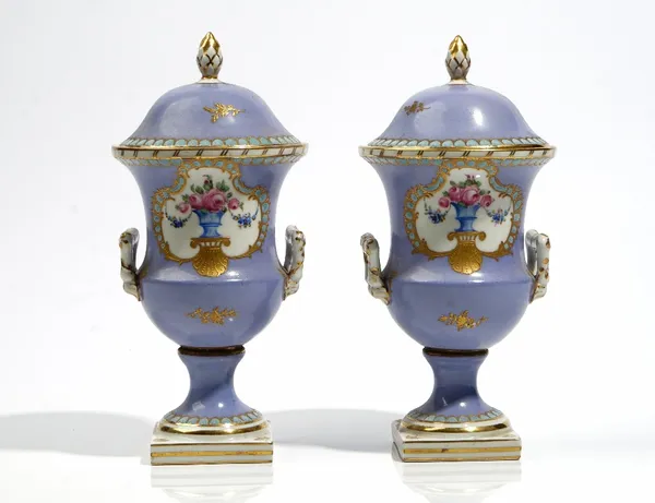 A pair of small French porcelain lilac-ground two-handled vases and covers, circa 1900, each painted with a vase of pink roses inside a gilt and turqu