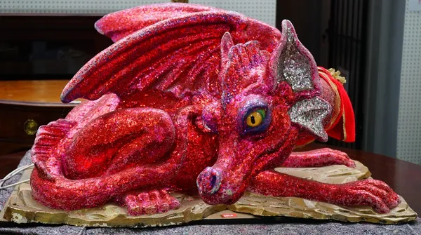 A fairground model of a dragon decorated in red and pink glitter, the head articulating, on a gold painted rocky base, 125cm x 100cm.