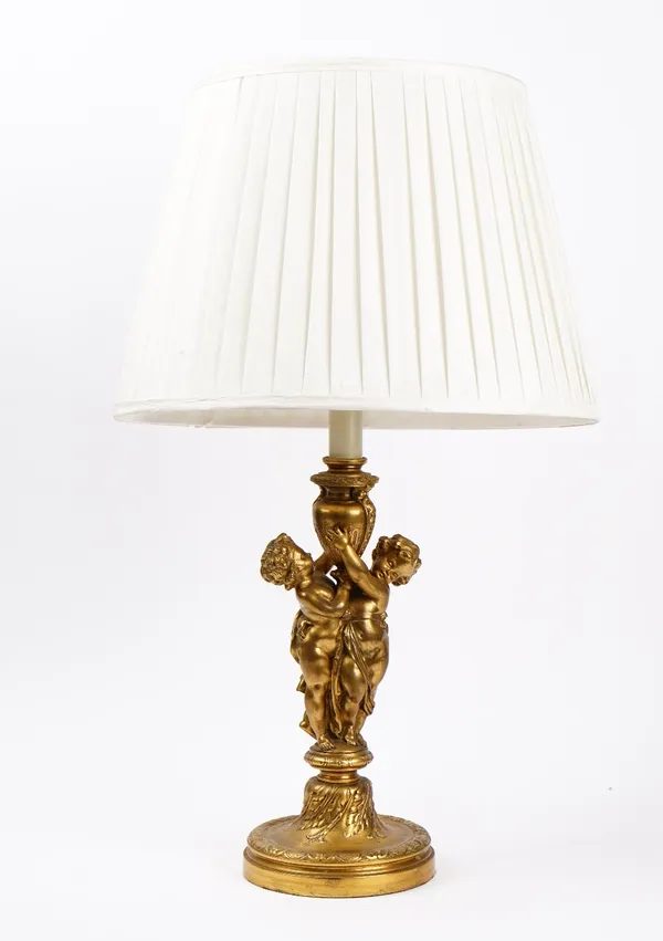 A French gilt metal candlestick, late 19th century, converted to a table lamp, modelled as two standing cherubs clutching a vase, 36cm high, with shad