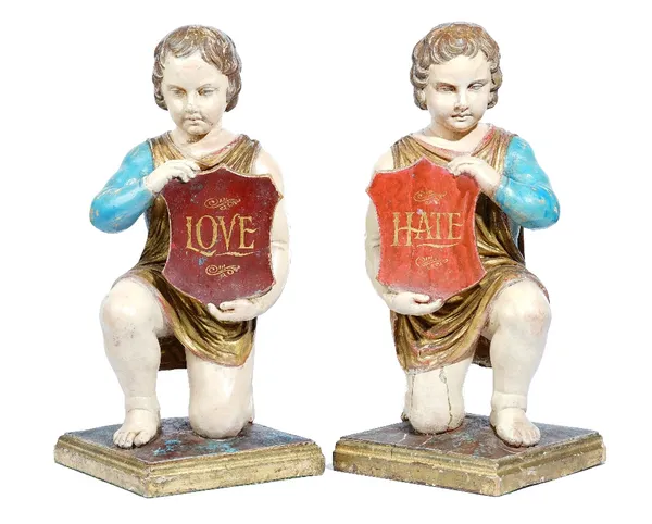 A pair of painted figures of kneeling cherubs, each holding a shield with gilt lettering "Love and Hate", on square bases, in the 18th century North I