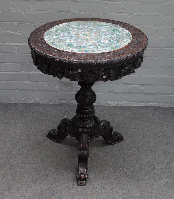 A 19th century Chinese export occasional table, the circular top inset with a ceramic famille verte panel, depicting interior scenes,.within a carved