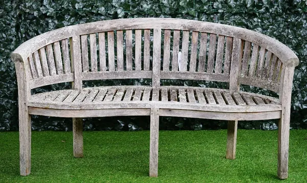 A teak semi-elliptic garden bench of slatted construction on block supports, 160cm wide x 87cm high