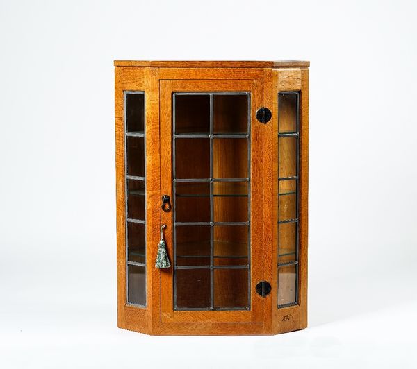 Robert Mouseman Thompson; A 20th century blonde oak hanging corner display cabinet with a trio of leaded glazed panels, 70cm wide x 97cm high.