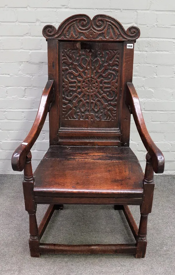 An oak Wainscot chair, 17th century and later, with a foliate carved arched top rail and panelled back, solid seat, on turned and square section legs,