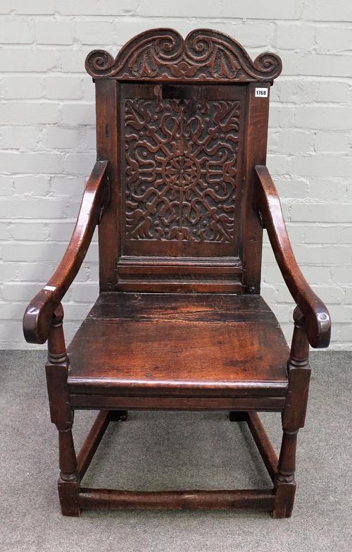 An oak Wainscot chair, 17th century and later, with a foliate carved arched top rail and panelled back, solid seat, on turned and square section legs,