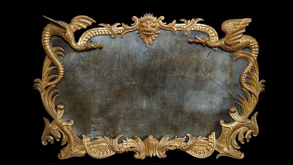 An 18th century gilt framed mirror, the foliate moulded shaped frame centered by three grotesque masks, flanked by dragons, 95cm wide x 62cm high.