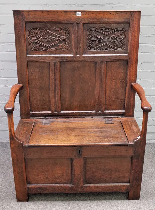 A 18th century oak box seat settle, with carved panel back and open arms, 96cm wide x 128cm high.