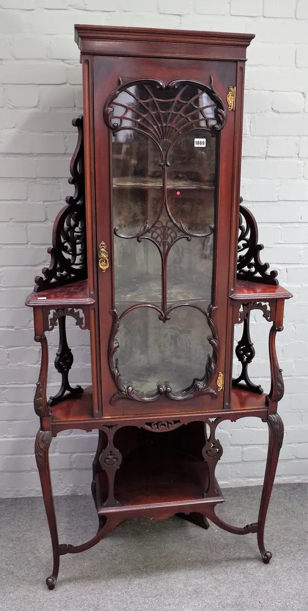 An Art Nouveau foliate carved mahogany floor standing corner cabinet, enclosed by a glazed door, flanked by open shelves and with undertier, 78cm wide