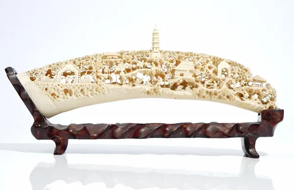 A Canton ivory tusk, early 20th century, intricately carved and pierced with figures, animals, buildings and trees and surmounted by a tiered pagoda,