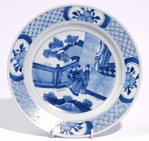 A Chinese blue and white plate in Kangxi style, painted with a figurative panel inside a diaper border reserved with panels of fruit, 22.5cm. diameter